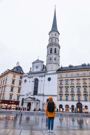 woman tourist in yellow raincoat with backpack looking at saint michaels church vienna austriaの写真素材