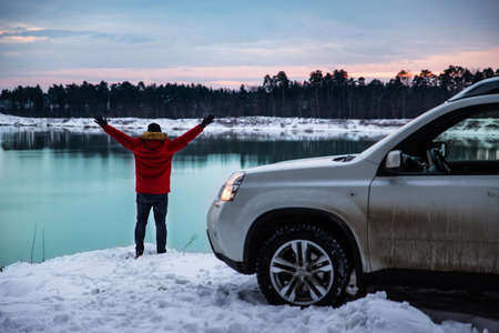 man near suv car at winter time. lake with forest on background. active lifestyleの写真素材