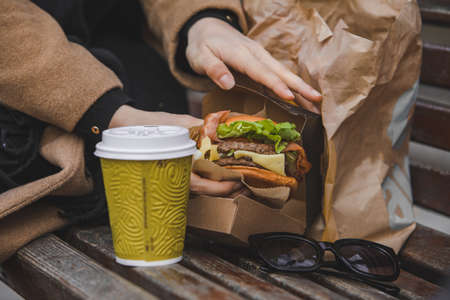 woman hands close up holding burger with coffee cup. fast food conceptの写真素材