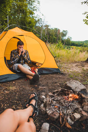 couple sitting near fire drinking tea from metal mugの写真素材