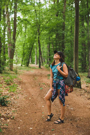 young adult woman walking with backpack by forest trail