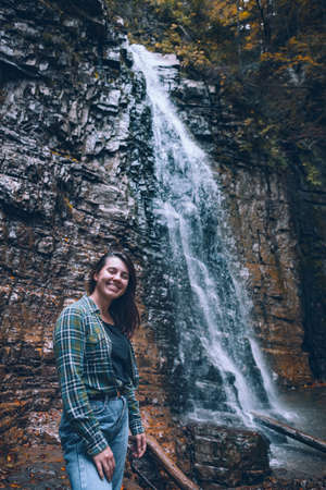 smiling woman in front of autumn waterfallの写真素材