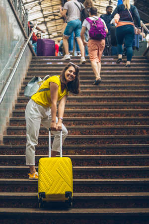 woman pulling up by stairs heavy yellow suitcase on wheelsの写真素材