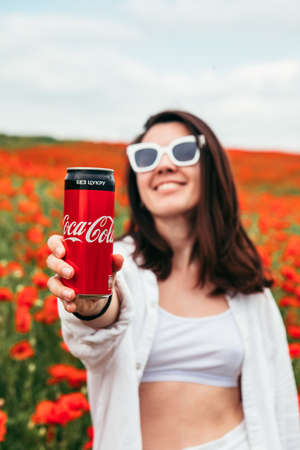 Lviv, Ukraine - Jun 11, 2020: Woman drinking coca cola standing at the field of poppy flowers. hot summer dayのeditorial素材