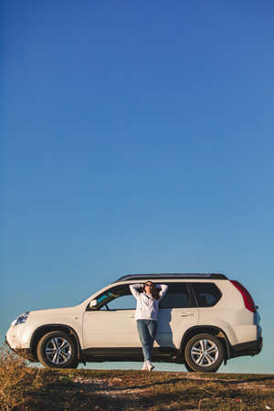 woman in casual clothes standing near white suv car road trip conceptの写真素材