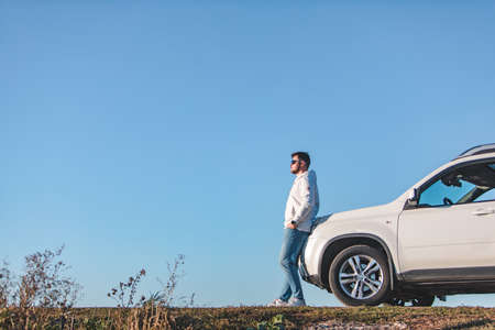 young adult man standing near car in sunglasses blue sky on backgroundの写真素材