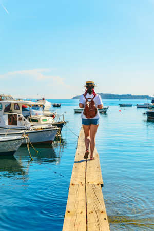 young pretty woman traveler at wooden dock in sea bay. boats on background