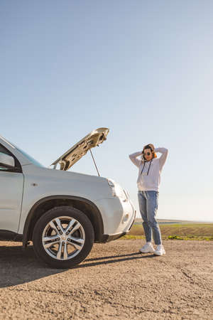 woman standing near car with opened hood on sunset
