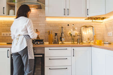 view from behind woman on kitchen cookingの写真素材
