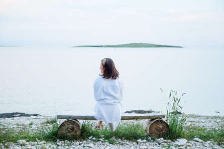 woman sitting on bench looking on sunset over the seaの写真素材