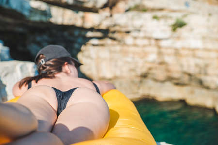sexy woman laying on air sofa sunbathing at sea rocky beach. summer vacation. copy spaceの写真素材