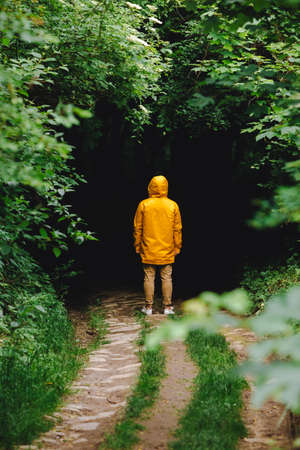 man in yellow raincoat sanding in front of dark entrance to the forest. copy space