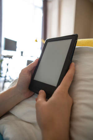 electronic book with empty screen in woman hands. laying in bed