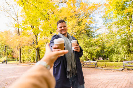 man brings coffee to friend drink to go outdoors autumn city parkの写真素材