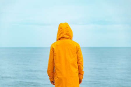 woman in yellow raincoat at sea beach cliff at storm rainy weather. summer vacation. travel concept. hikingの写真素材
