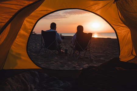 young adults couple looking on sunrise drinking coffee sitting in camping chair. lifestyle.の写真素材