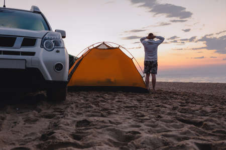 man standing near camping tent with suv car looking at sunrise. copy space. life styleの写真素材