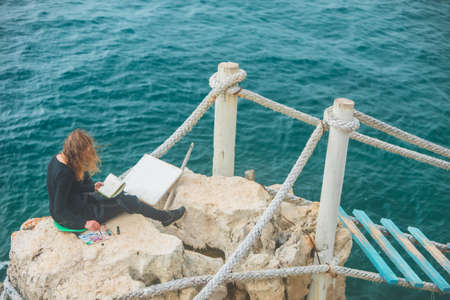 woman sitting at the edge drawing picture of seascape suspension bridgeの写真素材