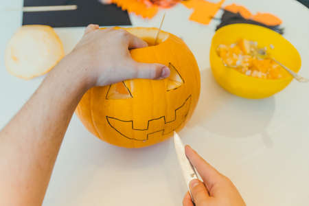 young father with toddler son making jack pumpkin head for halloween holiday