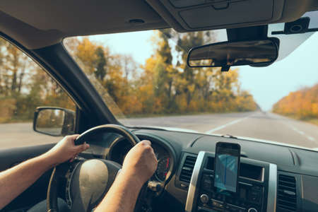 road trip concept man hands on steering wheel navigation on the phone autumn fall seasonの写真素材
