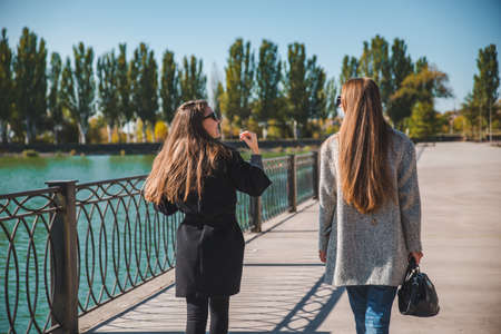two girlfriends walking by city quay in coats autumn fashion sunny day