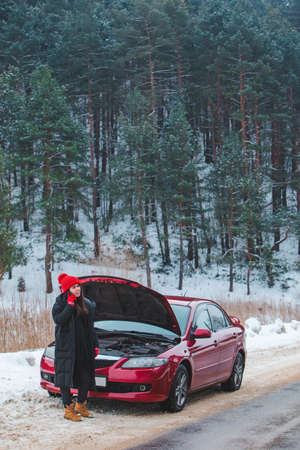 woman calling for help with broken down car at winter highway stopped at roadsideの写真素材