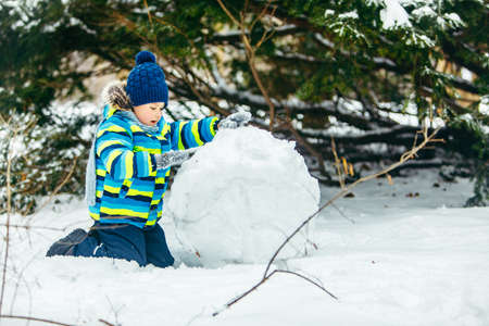 little cute boy making snowman. rolling big snowball. winter leisure