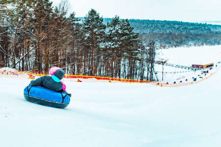 parent with kid sliding down by snowed hill with snowing tube. winter leisureの写真素材