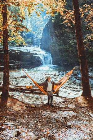 woman laying on hammock with view of autumn waterfall sunny warm day hiking conceptの写真素材