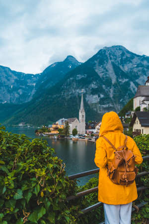 woman in yellow raincoat looking at hallstatt city panoramic viewの写真素材