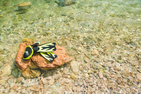 snorkeling mask with flippers at rock in sea water