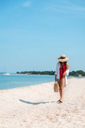 young stunning woman in red swimsuit walking by sea beach. summer outfitの写真素材