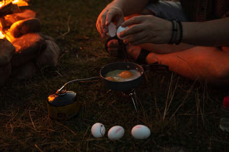man sitting near bonfire cooking fried eggs. copy space