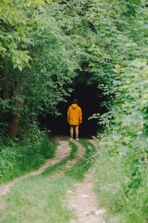 man in yellow raincoat sanding in front of dark entrance to the forest. copy spaceの写真素材