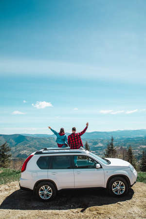 young woman sitting on the top of the suv car at mountain peak enjoying the landscape view at summer sunny dayの写真素材