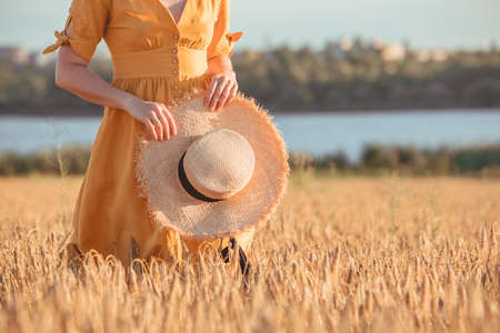 woman in yellow sundress walking by wheat field. summer timeの写真素材