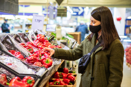 woman in medical mask do groceries shopping choosing sweet pepperの写真素材