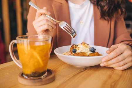 smiling beautiful woman in cafe eating cake with ice cream and blueberries orange tea in mugの写真素材