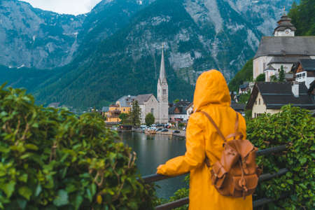 woman in yellow raincoat looking at hallstatt city panoramic viewの写真素材