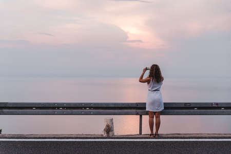 stop on the road woman taking picture on the phone of sunset above the sea copy space