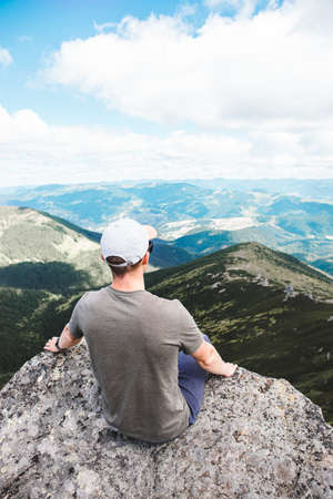 young strong man sitting on the rock at the top of the mountains peak enjoying the view. hiking conceptの写真素材