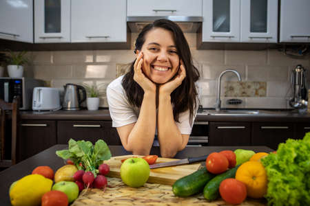portrait of beautiful smiling woman at the kitchen with fruits and vegetables on the table