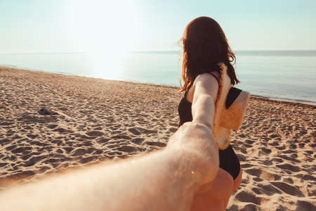 woman holding hand man. follow me concept. walking by sandy sea beach on sunsetの写真素材