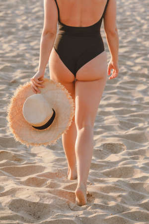 young pretty woman butt at sandy beach in black swimwear on sunset. summer vacationの写真素材