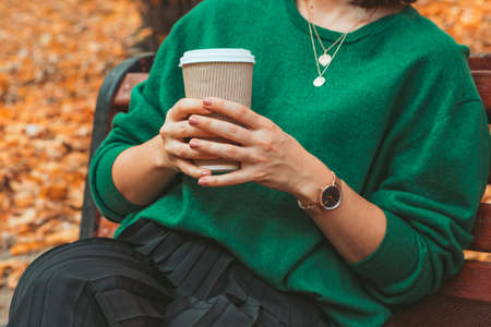 woman sitting on the bench at warm autumn day drinking coffee to go