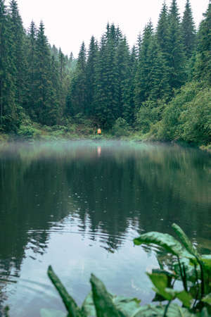 man hiker in yellow raincoat looking at mountain lake traveler concept copy spaceの写真素材