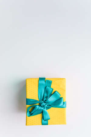 present gift box wrapped with yellow paper and blue ribbon top viewの写真素材