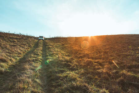 white suv car riding by trail road at the field on sunset. copy spaceの写真素材