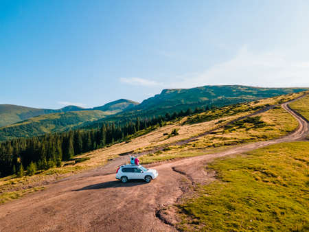 aerial view of couple sitting on the suv car roof enjoying view of carpathian mountains Ukraineの写真素材
