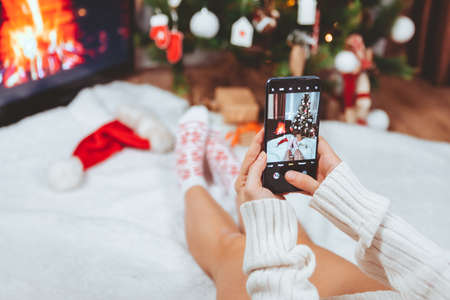 woman taking picture on the phone near christmas tree cozy placeの写真素材